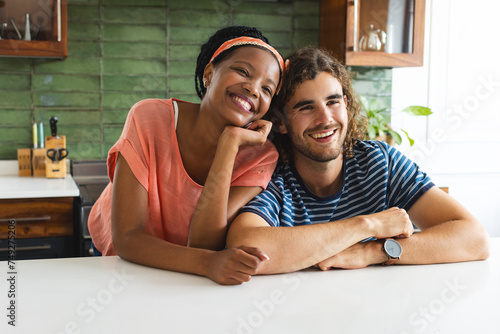 Diverse couple smiles warmly, leaning on a kitchen counter