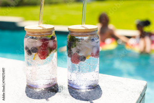 Two refreshing fruit-infused water jars with straws sit by a pool
