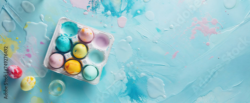 Light blue messy painted backdrop with smears, blobs and splashes, with flat lay colorful eggs in an egg carton and copy-space. Created with AI. photo