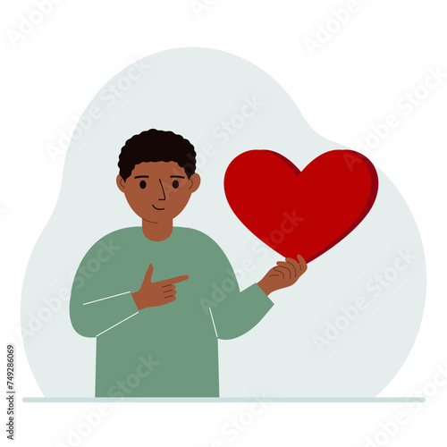 A boy holds a big red heart in his hand. The concept of volunteering, romantic relationship or love.