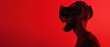 Silhouette of a male wearing a virtual reality headset, highlighted against a vibrant red backdrop forming a striking contrast