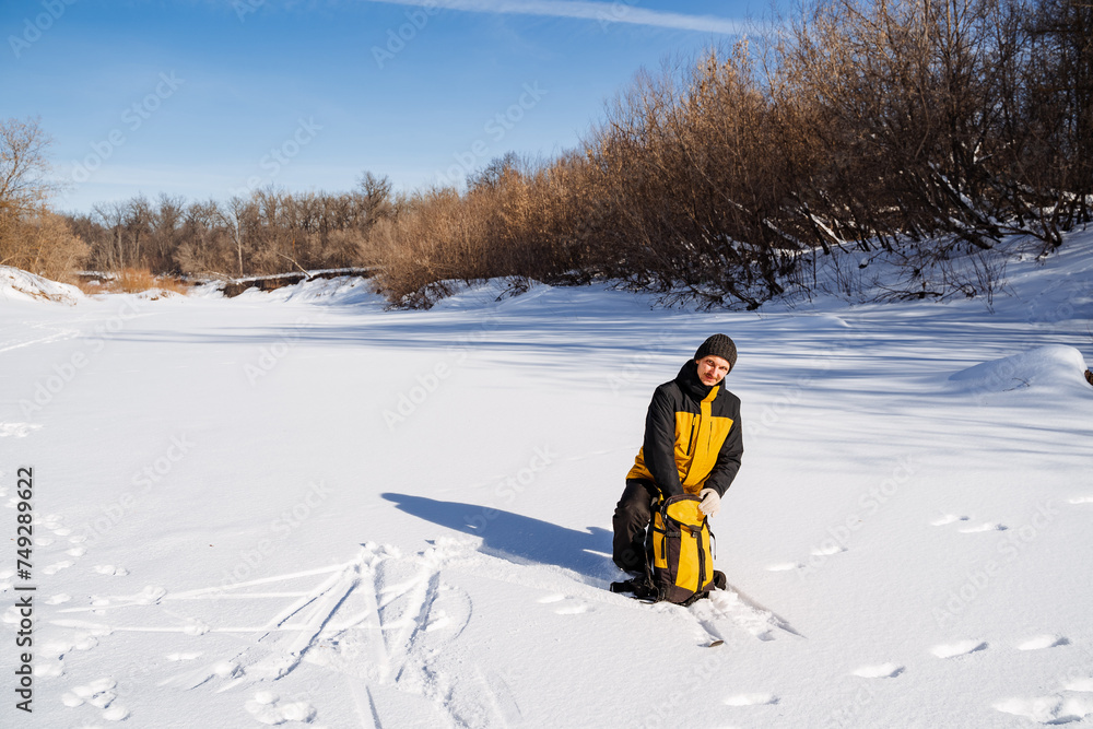 A man in a yellow jacket sits in the snow taking things out of a backpack, a solo journey through a winter forest.