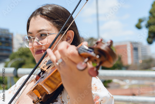 Photography portrait of young latin woman violinist making music on street