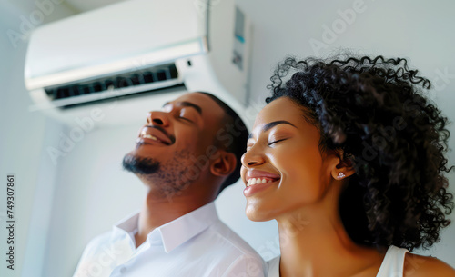 happy black young man and woman enjoying the coolness of the air conditioner in their home photo