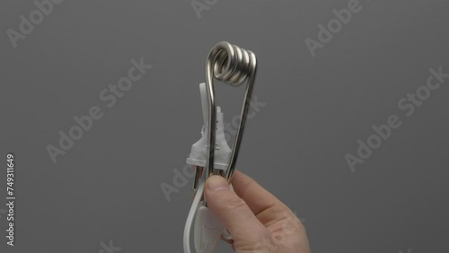 A travel immersible water heater rotates in a hand on a gray background.