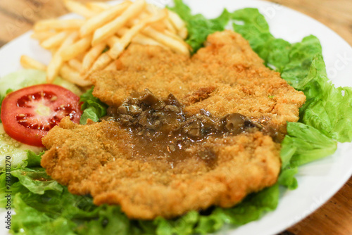 Chicken schnitzel served with mushroom sauce, french fries, lettuce, cucumber and tomato pieces