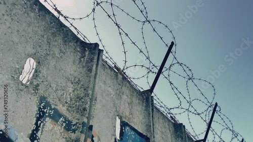 Restricted zone protected with high concrete wall and sharp barbed wire, horror cinematic shot of protected area, concentration camp or military zone, border line control to protect area from illegal