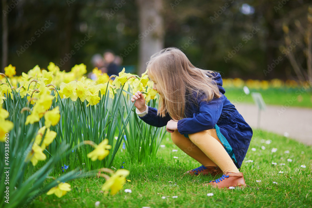 Fototapeta premium Adorable preschooler girl enjoying nice spring day in park during jonquils blooming season