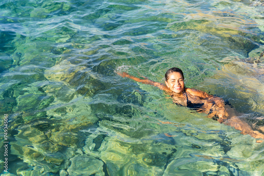 Beautiful woman enjoying a magnificent swim in transparent turquoise waters in the Aegean Sea on her vacation in Greece in summer