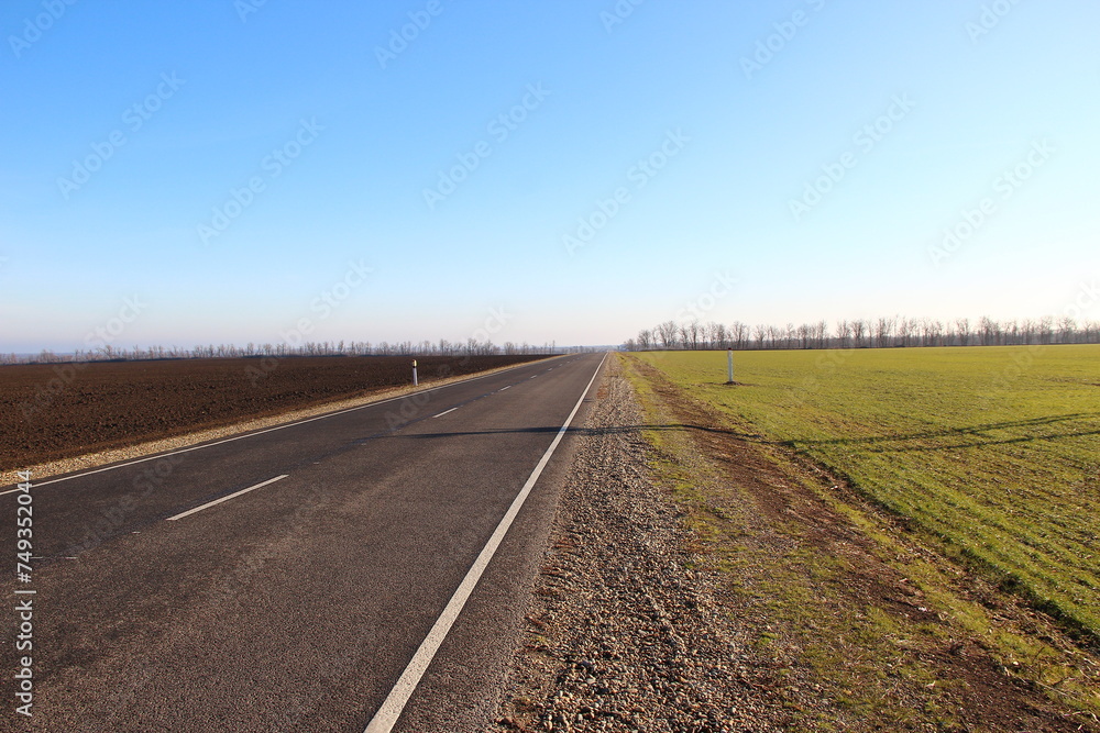 Asphalt road near agricultural fields and blue sky on a backround