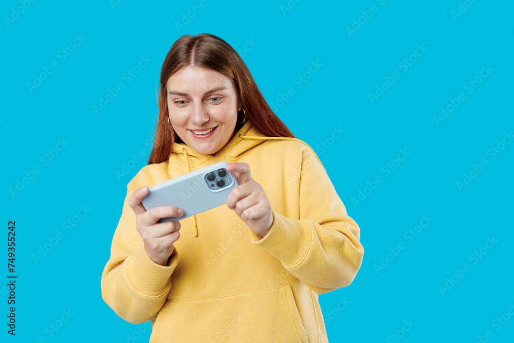Close up portrait of a Happy 30s woman playing games with a smart phone isolated on a blue background Close up portrait of a Happy 30s woman playing games with a smart phone isolated on a blue background