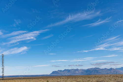 Panoramic view of the Hvannadalshnukur mountain range on the South Coast of Iceland with various glaciers seen from Þjóðvegur or Route 1 with feathered clouds in blue sky