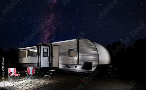 Milky Way rising over an RV with the entire campsite lighted at night.