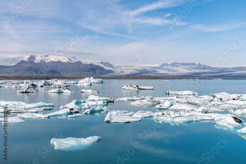 Panoramic view over the mirror like water of the glacial lagoon filled with icebergs of Fjallsarlon glacier in Iceland, part of Vatnajokull National Park with blue sky and feather clouds