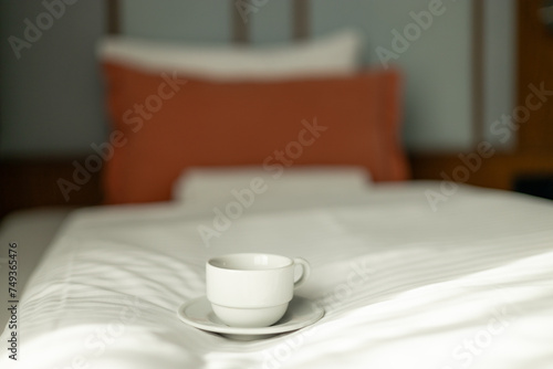 Coffee or tea cup on the bed. Hotel room or bedroom Interior, morning time. Concept of easy breakfast. One white ceramic cup.