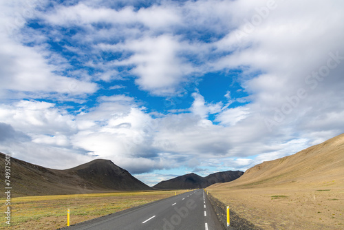 Panoramic view down a two lane road on Iceland, through the barren Icelandic Highlands with volcanos and mountains in the northern part of the country with a beautiful blue sky with white fluffy cloud © Sonja