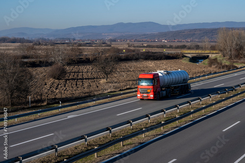 A red tank for the transport of fuel or hazardous materials drives on the highway through the beautiful rural area of ​​Serbia. 