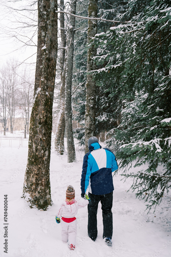 Dad and little girl walk through the snowy forest, holding hands under the snowfall