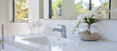 A modern bathroom sink with a ceramic basin and faucet sits on a white cabinet. In the basin  there is a clear vase filled with fresh flowers adding a touch of nature to the sleek  contemporary space.