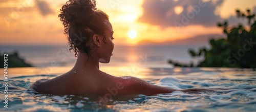 A woman is calmly seated in the water during sunset  taking in the evening colors and peaceful atmosphere.