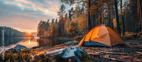 A tent is set up on the sandy shore of a tranquil lake  surrounded by trees and mountains in the background.