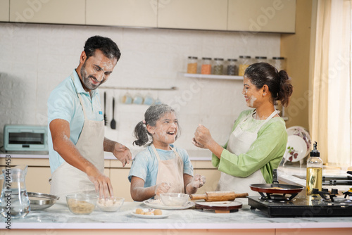 Playful Indian family with daughter plying flour while cooking at kitchen - concept of having fun, weekend holidays and relationship bonding photo