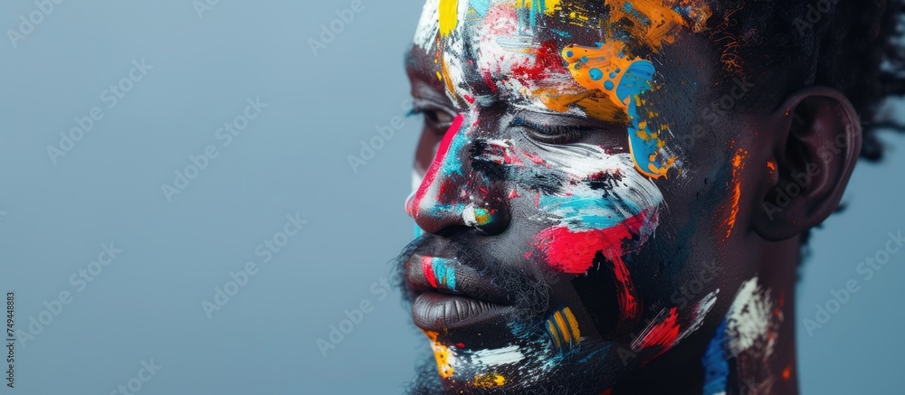 An African mans face is covered in a myriad of vibrant colors, showcasing intricate traditional face paint that seamlessly blends into abstract ink brush strokes in a unique art form known as An African mans face is covered in a myriad of vibrant colors, showcasing intricate traditional face paint that seamlessly blends into abstract ink brush strokes in a unique art form known as