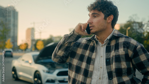 Stressed Caucasian man talking mobile phone on broken car open bonnet background road accident worried sad male driver automobile owner calling auto assistance services tow truck emergency help repair