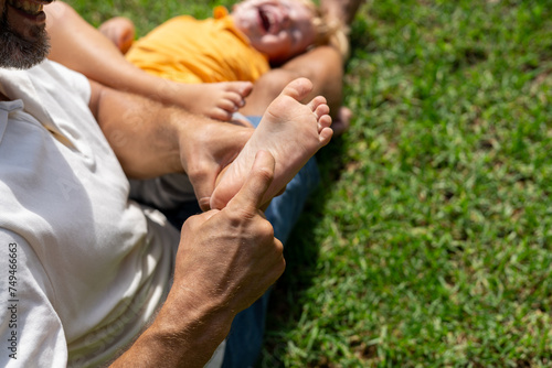 family and love concept - young father tickling his little son in park. close-up of a child's heel and the father's hand who tickles him. cheerful baby laughs from being tickled