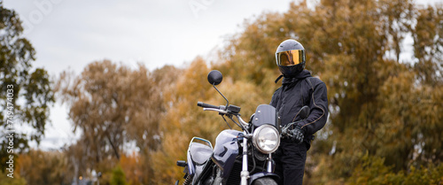 motorcyclist in a motorcycle jacket and tinted helmet with a classic motorcycle in nature. Stylish biker photo