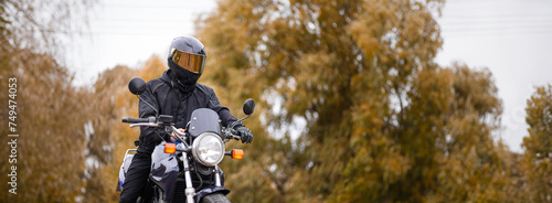 Schilderij op canvas motorcyclist in a motorcycle jacket and tinted helmet with a classic motorcycle in nature