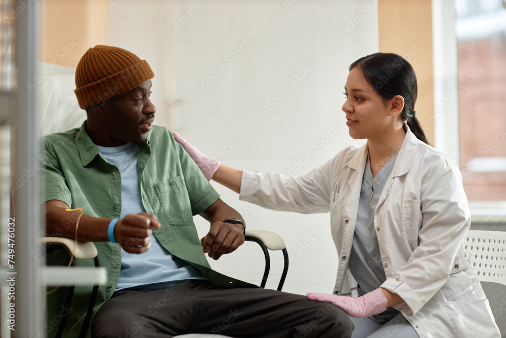 © Seventyfour - Side view portrait of smiling female doctor comforting patient receiving IV treatment in clinic