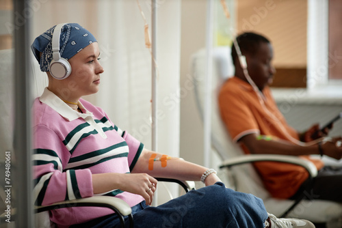 Side view portrait of two people getting chemotherapy treatment in clinic while sitting in chairs with IV drip tubes copy space photo