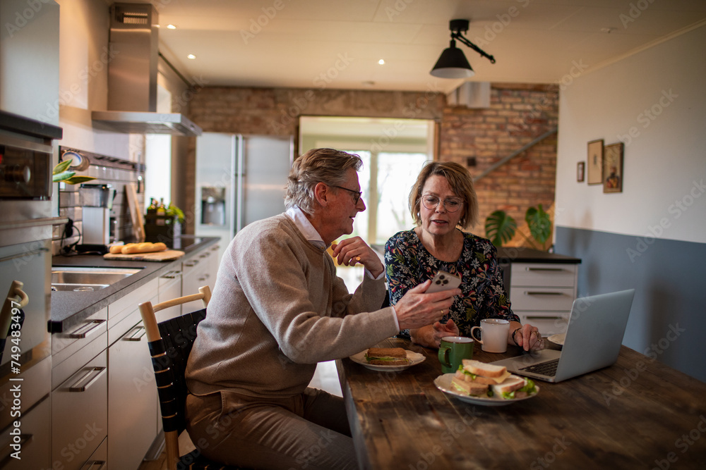 Senior couple eating breakfast with laptop in the kitchen Senior couple eating breakfast with laptop in the kitchen