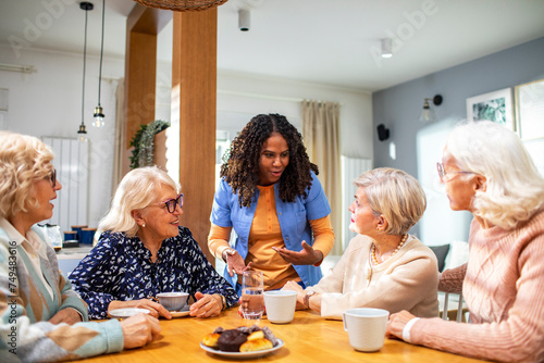 Group of senior women talking to caregiver at home kitchen table photo