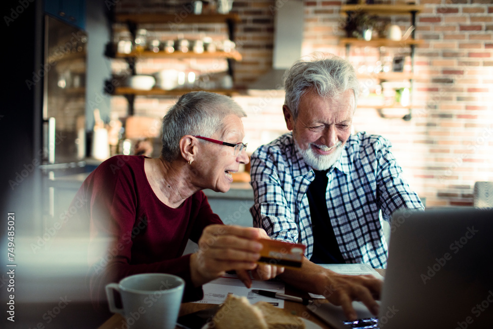 Smiling senior couple using credit card on laptop at home Smiling senior couple using credit card on laptop at home