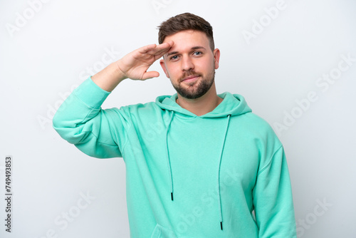 Young caucasian man isolated on white background saluting with hand with happy expression