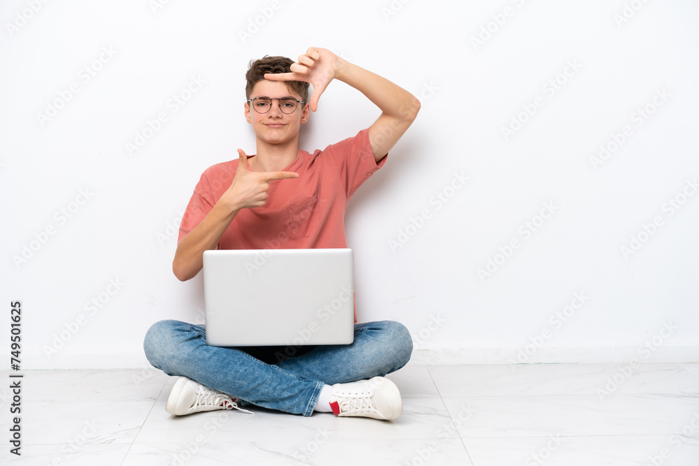 Teenager Russian man holding pc sitting on the floor isolated on white background focusing face. Framing symbol Teenager Russian man holding pc sitting on the floor isolated on white background focusing face. Framing symbol