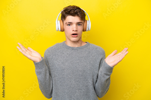 Teenager Russian man isolated on yellow background surprised and listening music