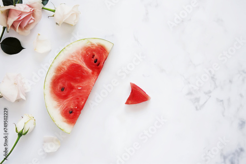 slice of watermelon with a small piece cut out, alongside elegant white and pink roses on a marble background.