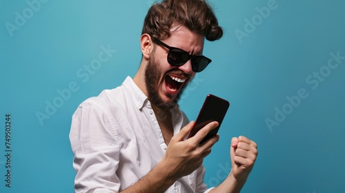 Cheerful young man in sunglasses using mobile phone isolated over blue background. Online Casino and Betting Concept with Copy Space. Gambling Concept.