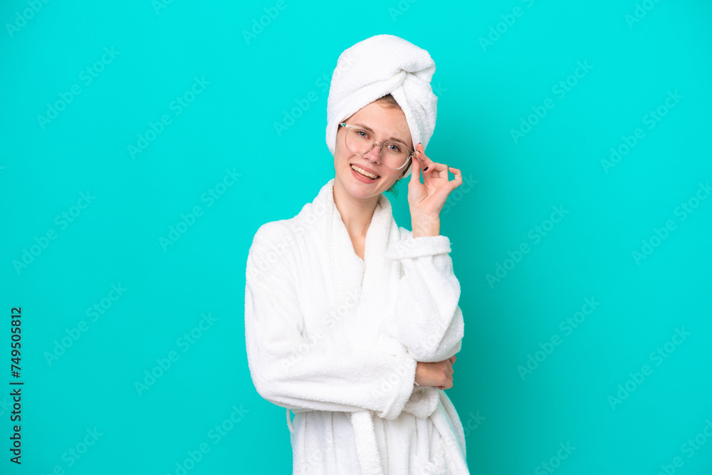 Young woman in a bathrobe isolated on blue background with glasses and happy Young woman in a bathrobe isolated on blue background with glasses and happy