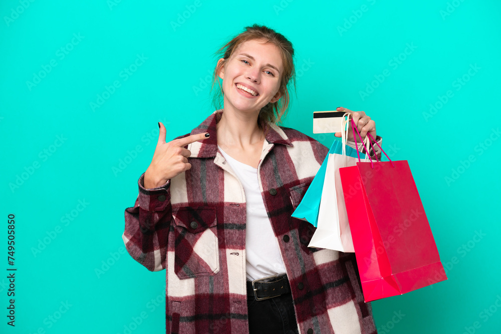 Young English woman isolated on blue background holding shopping bags and a credit card Young English woman isolated on blue background holding shopping bags and a credit card
