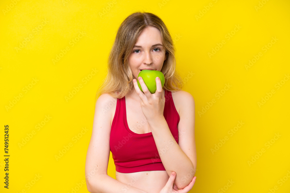 Blonde English young girl isolated on yellow background eating an apple Blonde English young girl isolated on yellow background eating an apple