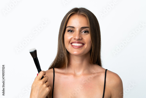 Young Uruguayan woman isolated on white background holding makeup brush and whit happy expression