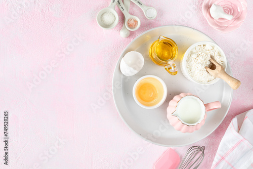 Baking ingredients and kitchen utensils on a pink background, top view.