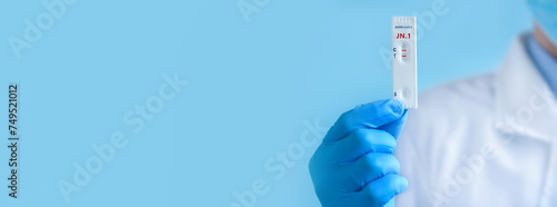 A doctor wearing a protective mask and gloves shows rapid laboratory test for Covid-19 New Variant JN.1 strain to detect IgM and IgG antibodies to the new coronavirus. Positive result. Banner photo