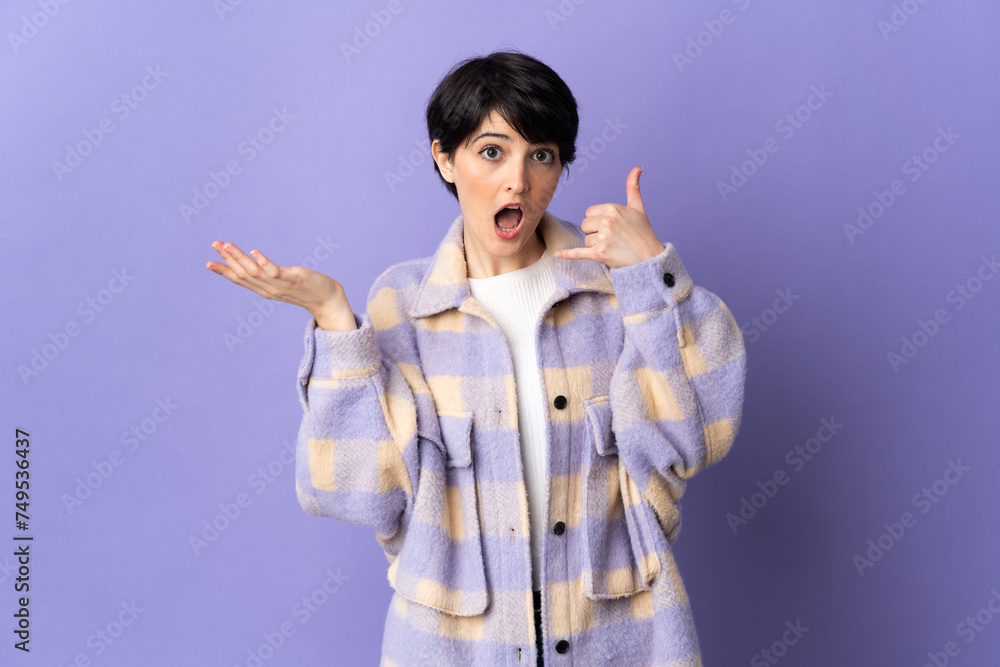 Woman with short hair isolated on purple background making phone gesture and doubting Woman with short hair isolated on purple background making phone gesture and doubting