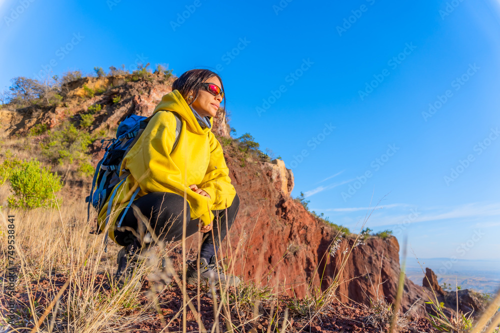 Naklejka premium woman in the mountains, with backpack and a yellow jacket, motivated by exploring new places. Concept: trekking, freedom, travel, exploration, motivation