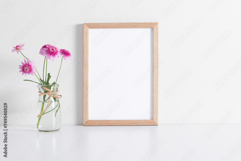 Blank frame mockup with pink flowers on table on white wall background. Empty frame mockup. Blank frame mockup with pink flowers on table on white wall background. Empty frame mockup.